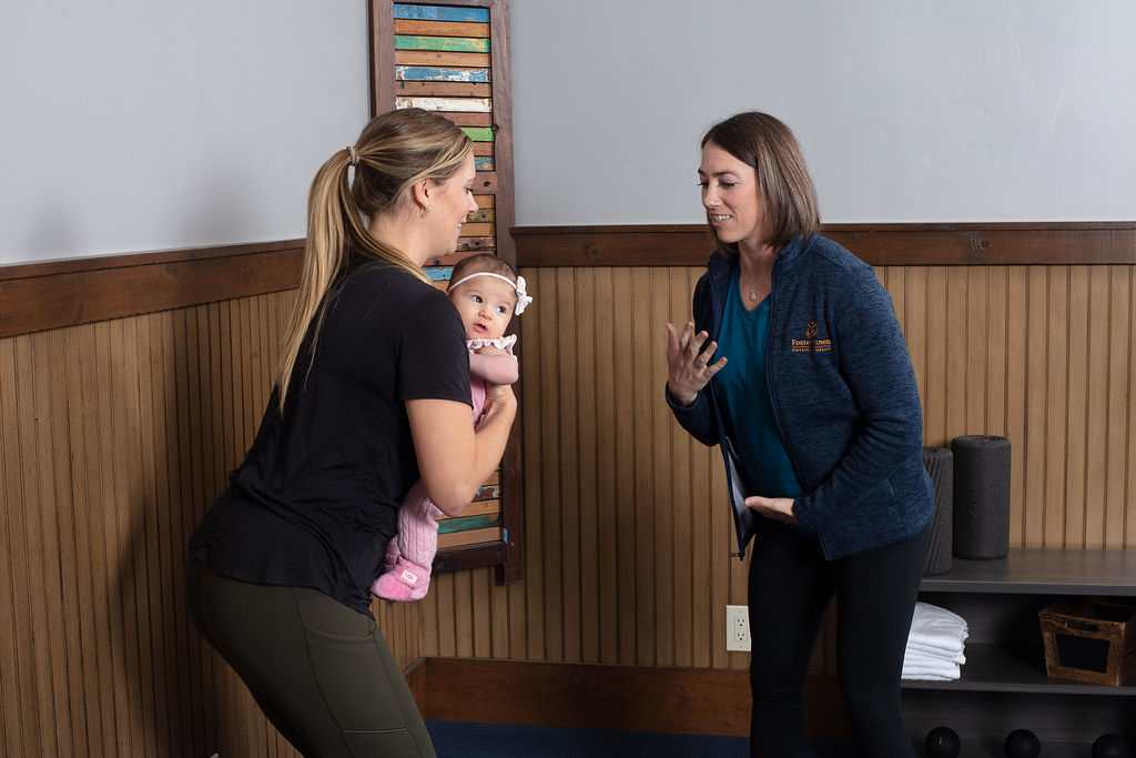 A physical therapist coaching a new mother holding her baby